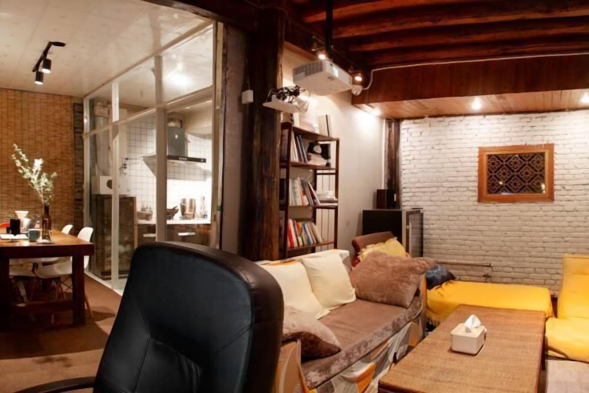 A cozy living room with a sofa, a coffee table, a bookshelf, and a dining area with chairs.