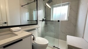A modern bathroom with a glass shower enclosure, a toilet, a sink with a towel, and a large mirror.