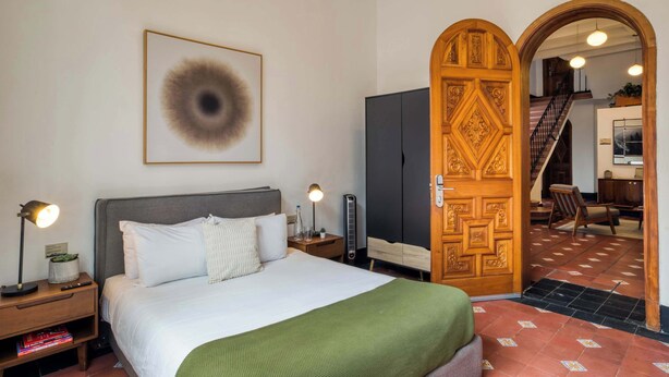 Habitación de hotel con cama, lámparas de noche, un cuadro enmarco, armario y puerta de madera.