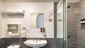 Un baño con lavamanos blanco, inodoro, cabina de ducha de vidrio y un perchero para toallas.