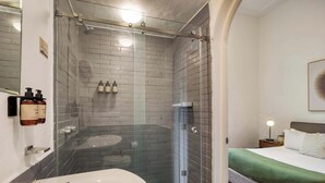 Un baño moderno con ducha de vidrio, un lavamanos blanco y una cama con colcha verde.