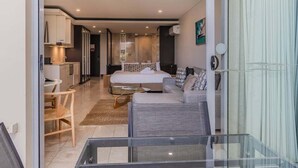 Un appartement moderne doté d’un balcon en verre, d’une cuisine avec des meubles blancs, d’un coin repas et d’un salon avec un canapé et un lit.