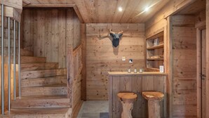 Et træpanelt interiør med trappe, et gevir og en bar med barstole.