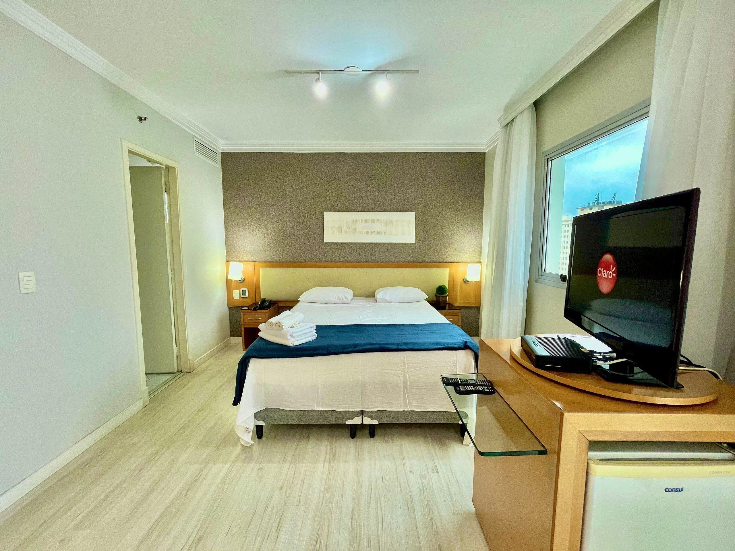 A hotel room with a bed, bedside tables, a television, and a window.
