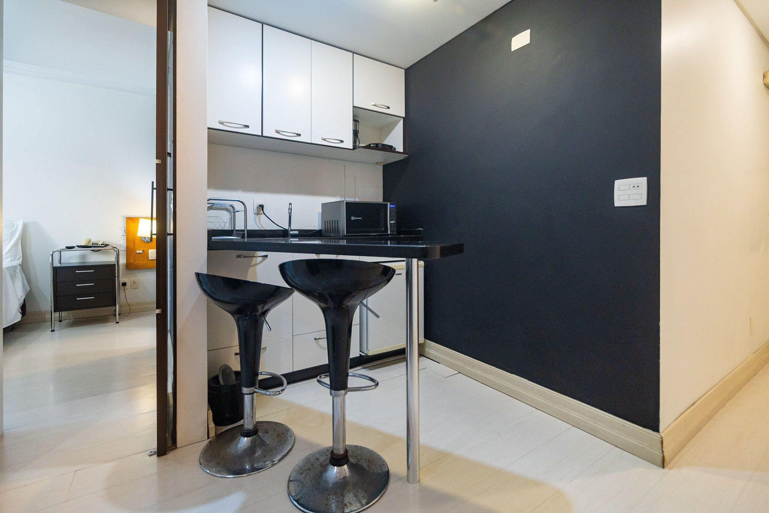 Una cocina compacta con armarios blancos, un microondas y dos taburetes de bar.