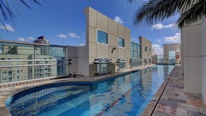 A swimming pool with clear blue water, surrounded by a modern building with large windows and a tiled deck. - LFlats Hotel Oscar Freire Hosp. Clínicas (São Paulo)