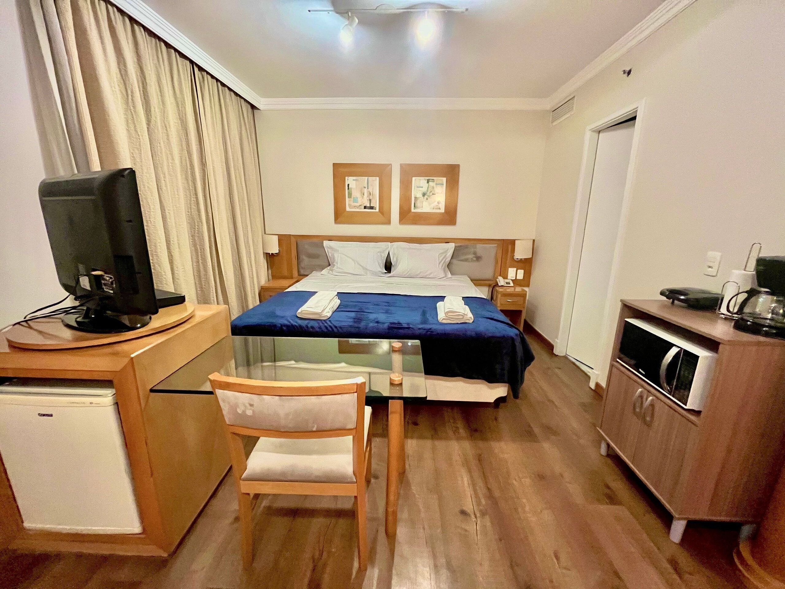 Habitación de hotel con cama, escritorio con computadora, silla, refrigerador pequeño y microondas.
