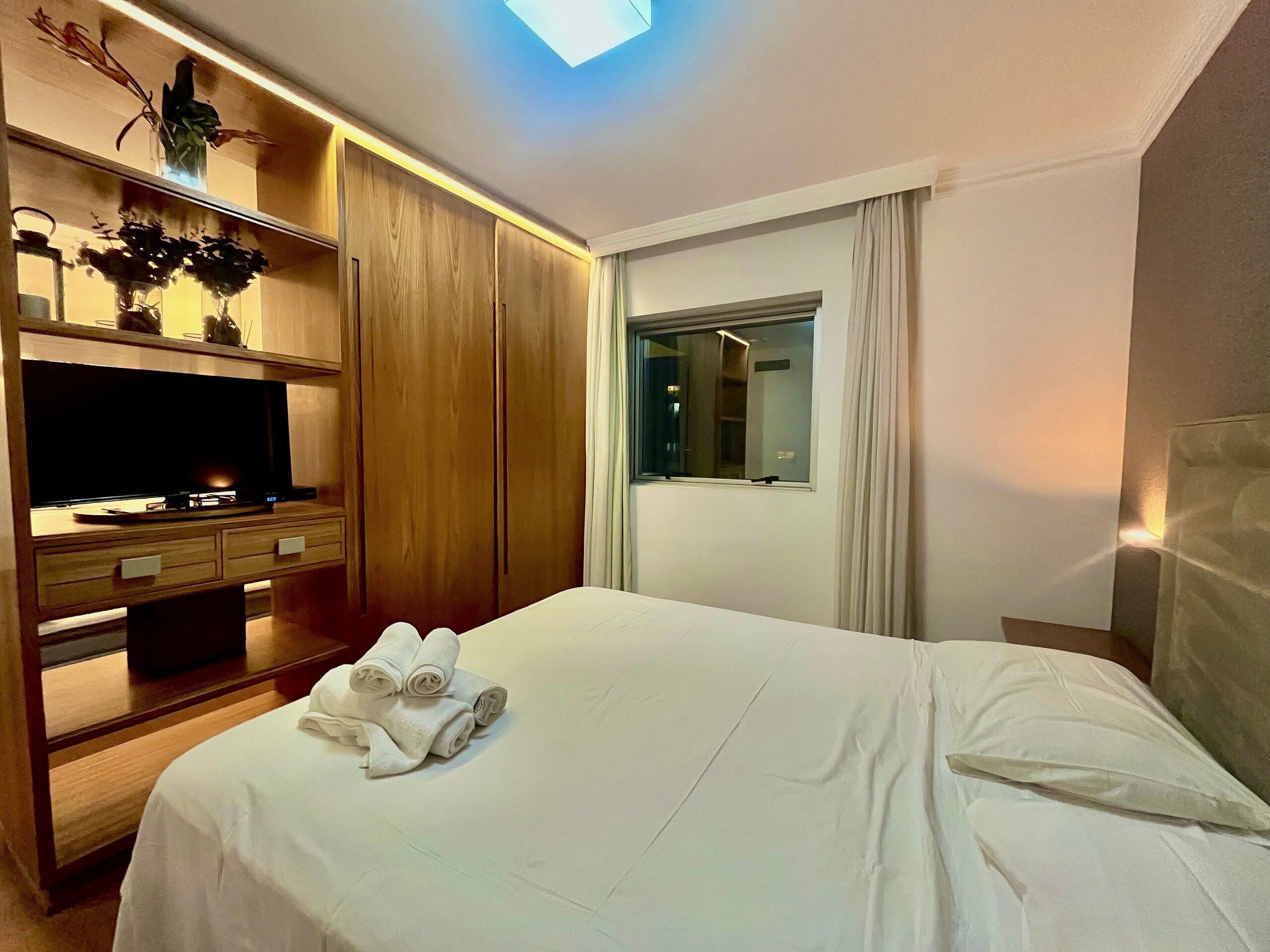 Quarto de hotel com cama, televisão, guarda-roupa e janela.