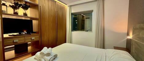 Quarto de hotel com cama, televisão, guarda-roupa e janela.