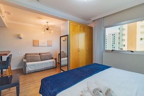 Une chambre d’hôtel comprenant un lit, un canapé, un bureau, un miroir et une fenêtre donnant sur la ville.