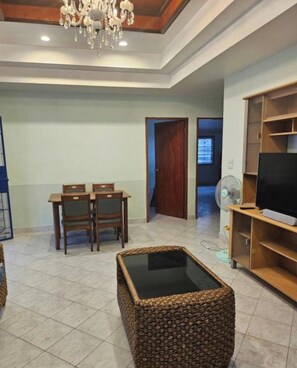 A living room with a dining table, chairs, a TV stand, and a fan. - Room in Guest Room - Room 2 in a Superb House in Exceptional City Center (Pattaya)