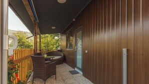 An outdoor patio area with a wicker table and chairs, a wooden fence, and a view of trees and a house in the background. - Glorija Riverside Retreat Near Olimje (kozje)