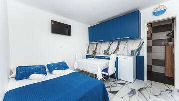 Une chambre d’hôtel comprenant un lit, une petite table avec une chaise, une kitchenette et un téléviseur fixé au mur.