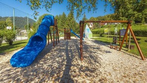 A playground with a blue slide, swings, and climbing structures. - Glorija Riverside Retreat Near Olimje (kozje)