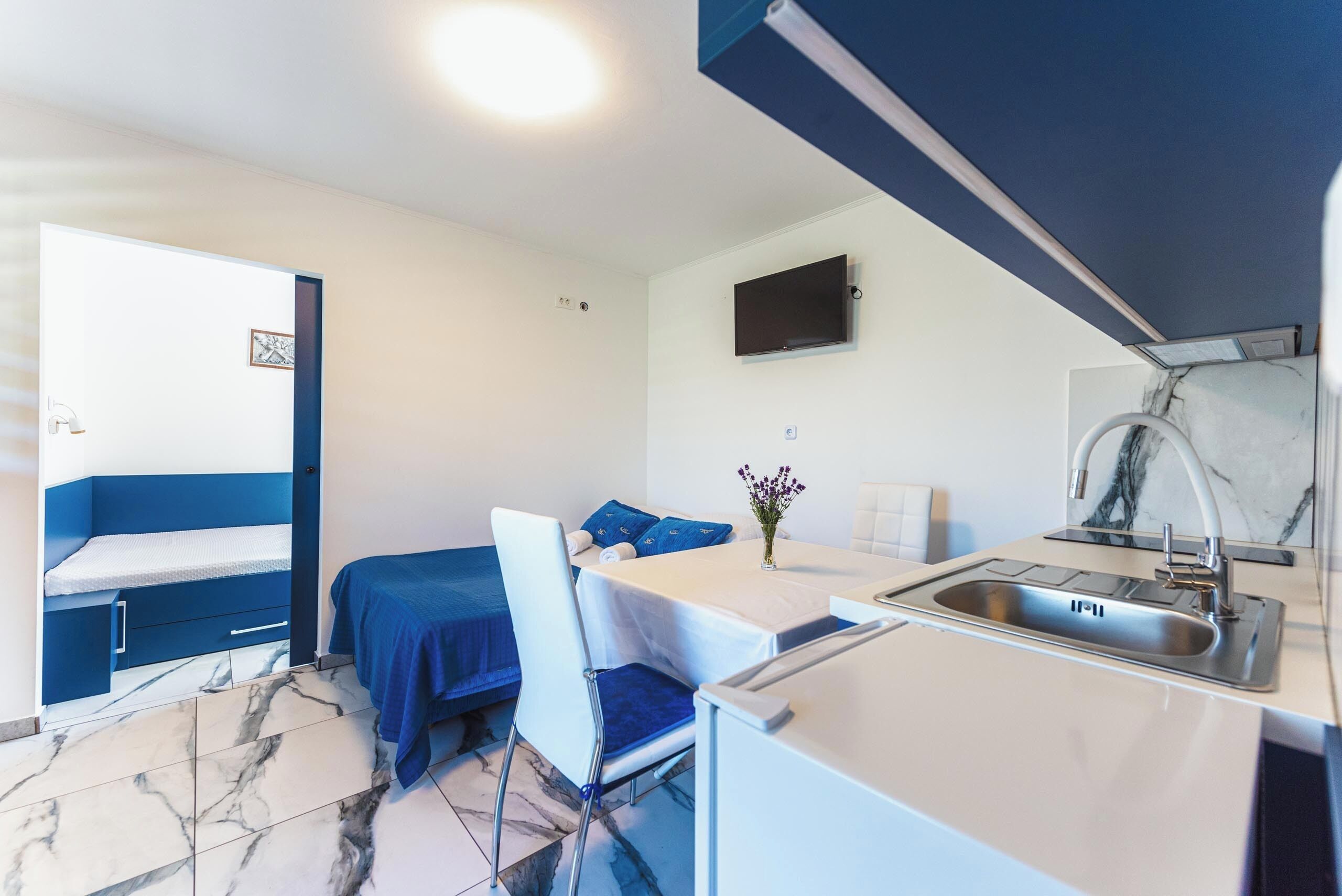 A compact room with a bed, a small table, a chair, a sink, and a television.