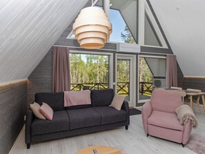 Une chambre de style loft moderne, dotée d’une grande fenêtre, d’un canapé gris foncé, d’un fauteuil rose et d’un luminaire en bois suspendu au plafond.