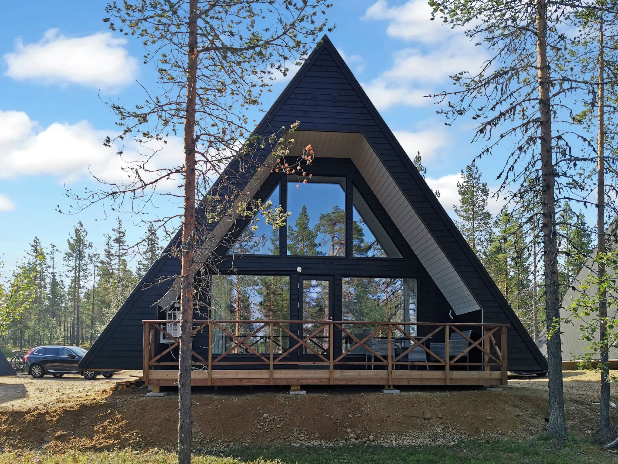 A triangular cabin with a wooden deck and large windows, surrounded by trees.