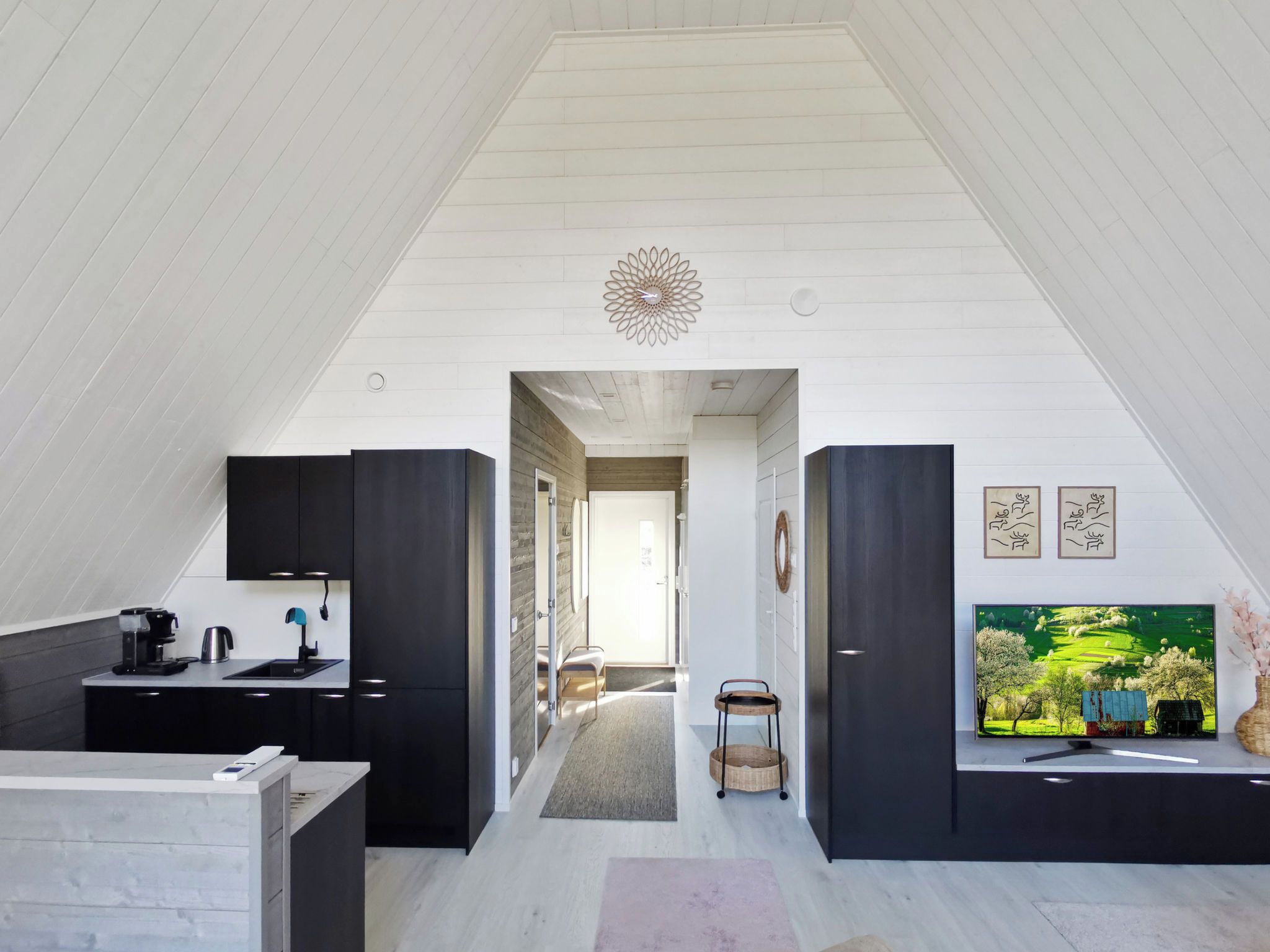 A modern loft with a sloped ceiling, a kitchen area with dark cabinetry, a dining space, and a large flat-screen TV mounted on the wall.