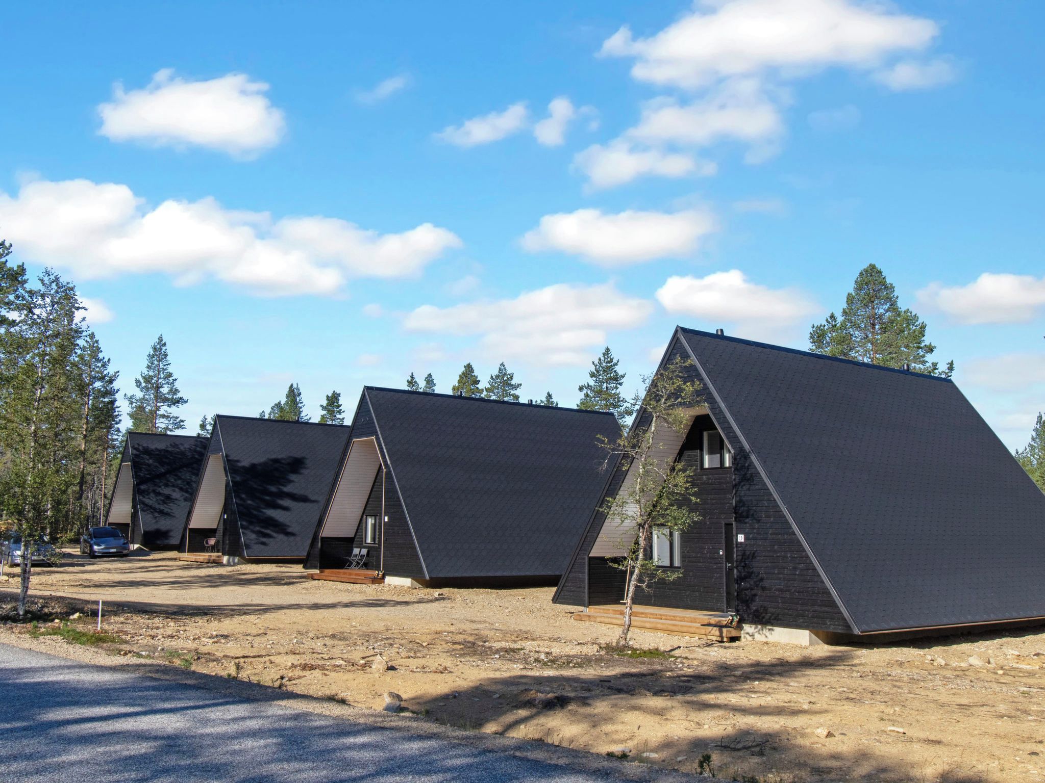 Une rangée de cabanes modernes, dotées de toits triangulaires, avec un sol en terre et une végétation clairsemée.