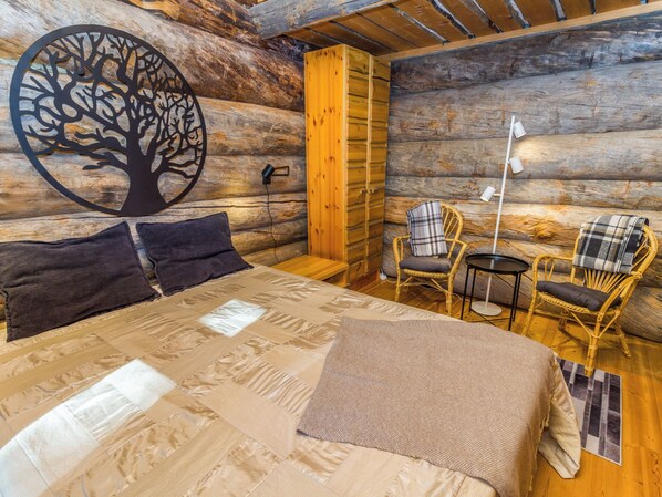 A log cabin room with a bed, two chairs, a table, and a wall art piece.