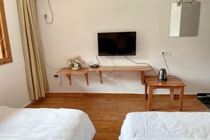 Una habitación con dos camas, un televisor en un estante de madera, una mesita con un hervidor y un espejo en la pared.