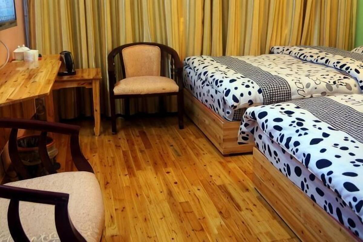 Una habitación con piso de madera, un escritorio con silla, una cama con ropa de cama estampada y un ventanal cubierto por cortinas.