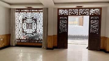 A room with a large window, a wooden door with intricate carvings, and a tiled floor.
