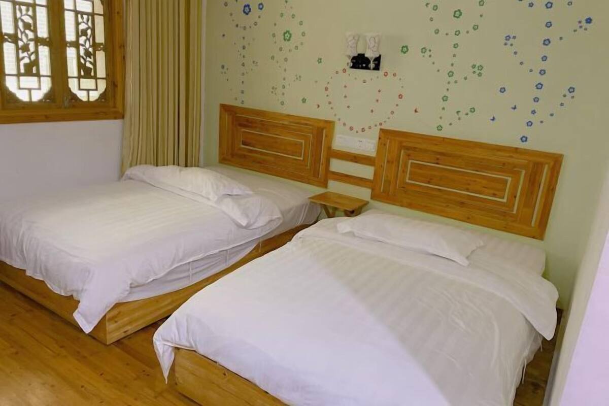 Una habitación con dos camas de madera, una ventana con marco de madera y una pared con estampado floral.
