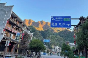 A street view with traditional architecture, a mountain in the background, and directional signs. - Tianzishan Inn (Zhangjiajie)