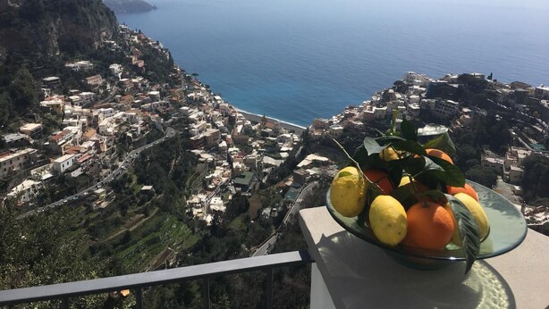 A coastal town with a view of the sea and a balcony with a fruit bowl.