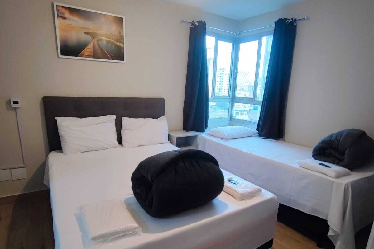 Een hotelkamer met een groot bed, een kleiner bed, een raam met gordijnen en een schilderij aan de muur.
