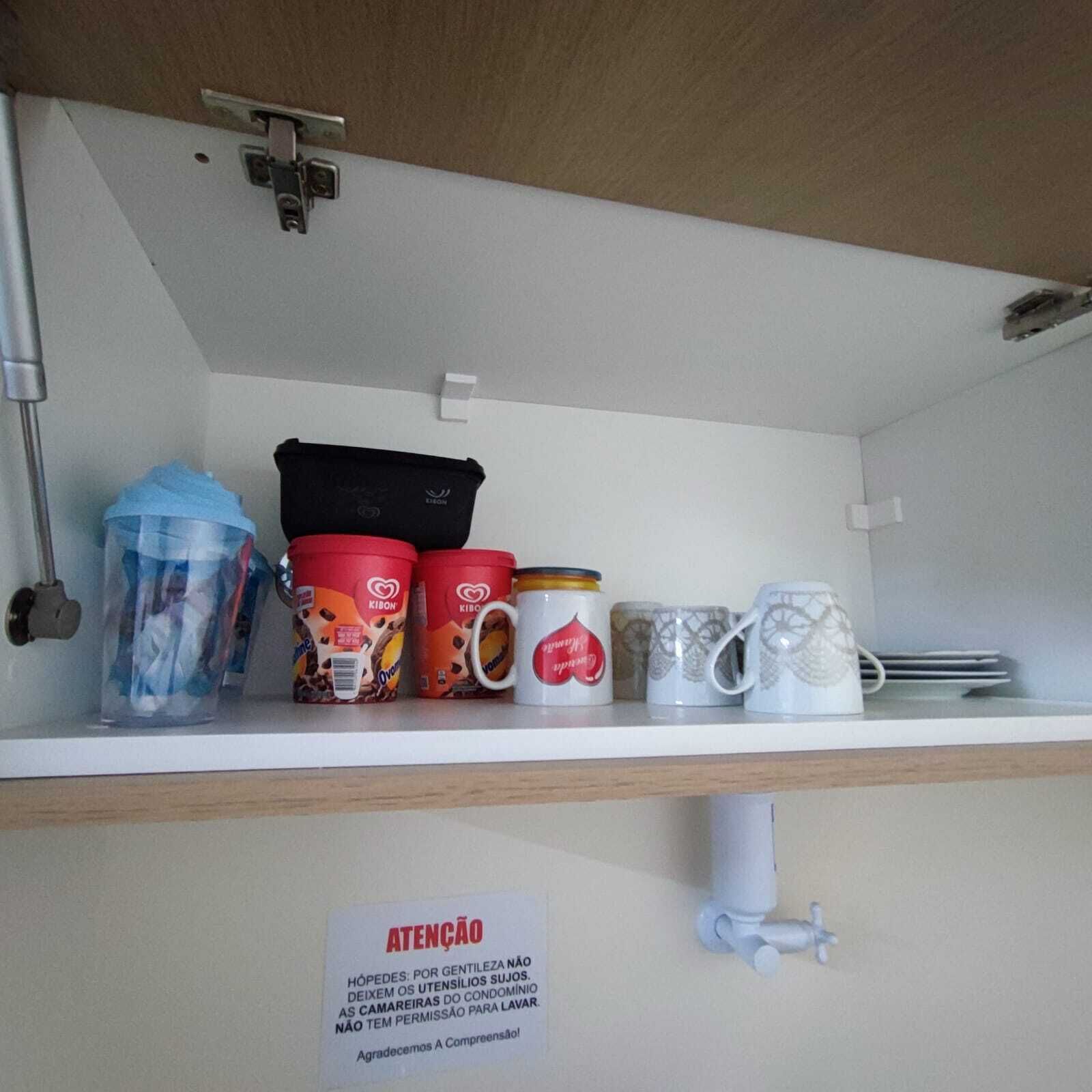 A shelf with various mugs and containers, a sign with a warning, and a water dispenser.