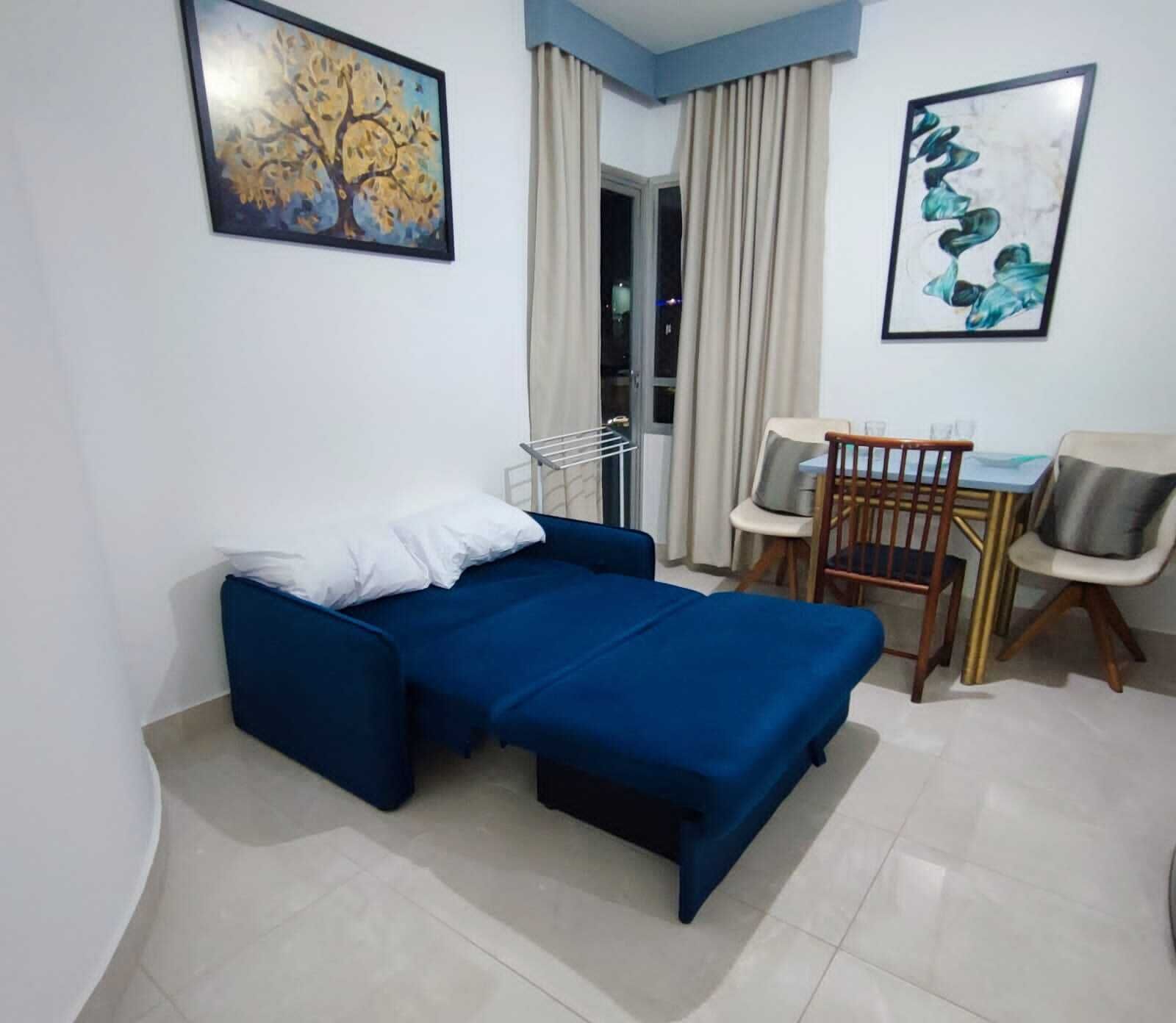 A room with a bed, a chair, a table, and two paintings on the walls.