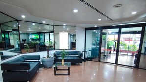 Een moderne lobby met een zithoek, een receptiebalie en een glazen deur naar buiten.