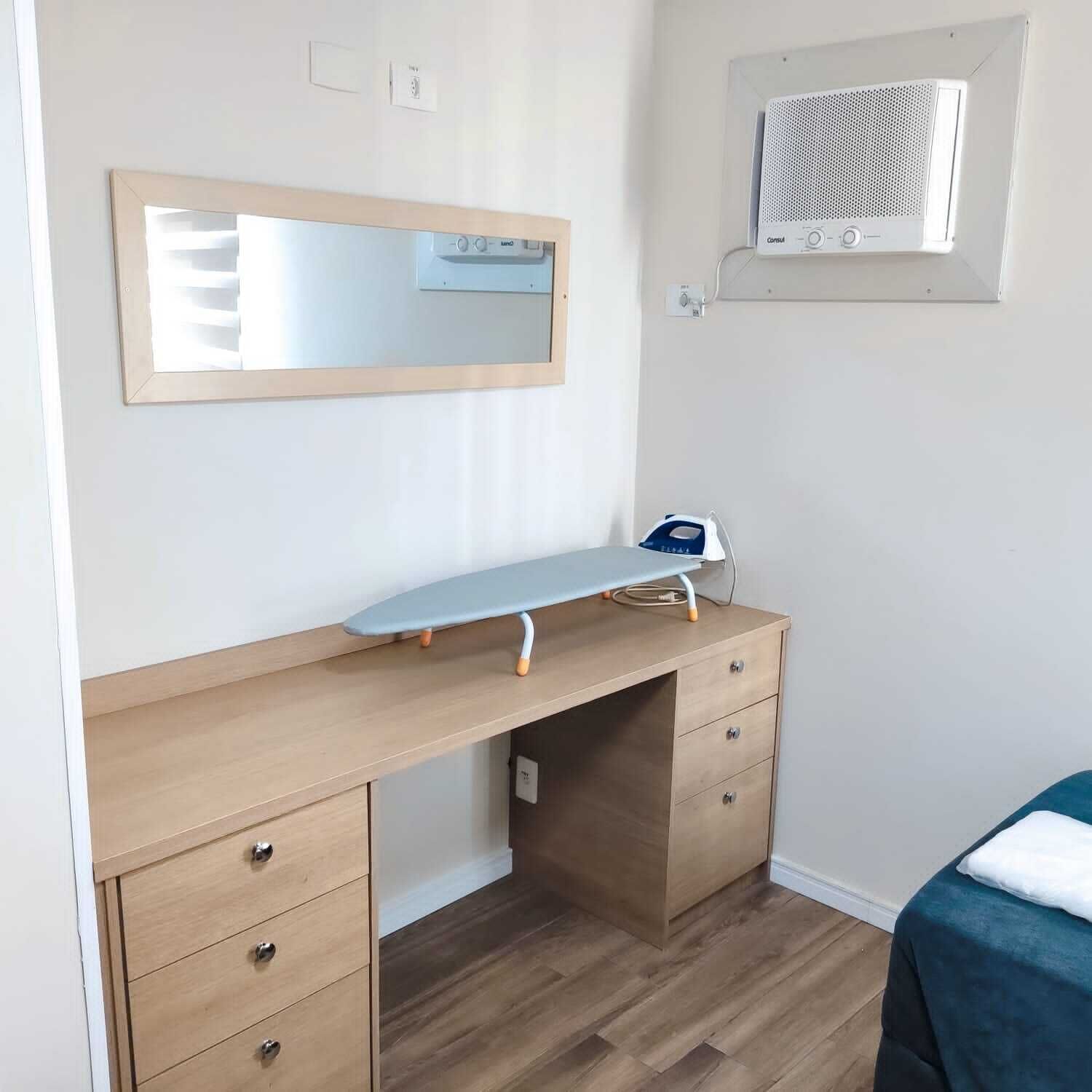 A bedroom with a wooden desk, a mirror, a small heater, and a bed with a blue cover.