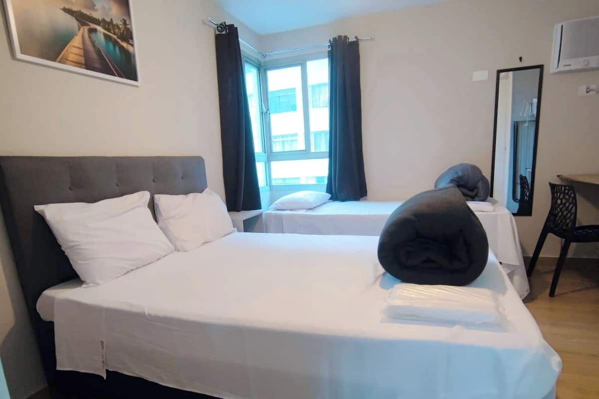 Een hotelkamer met twee bedden, een groot raam met gordijnen, een flatscreen televisie en een schilderij aan de muur.