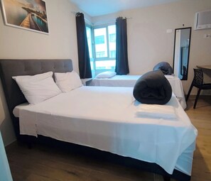 Habitación de hotel con dos camas, un ventanal con cortinas, un televisor de pantalla plana y un cuadro en la pared.