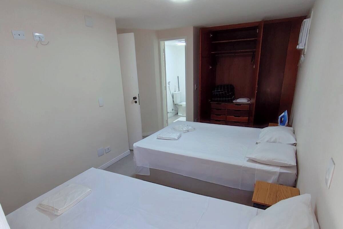 Een slaapkamer met twee bedden, een houten garderobe en een badkamer die door een open deur zichtbaar is.