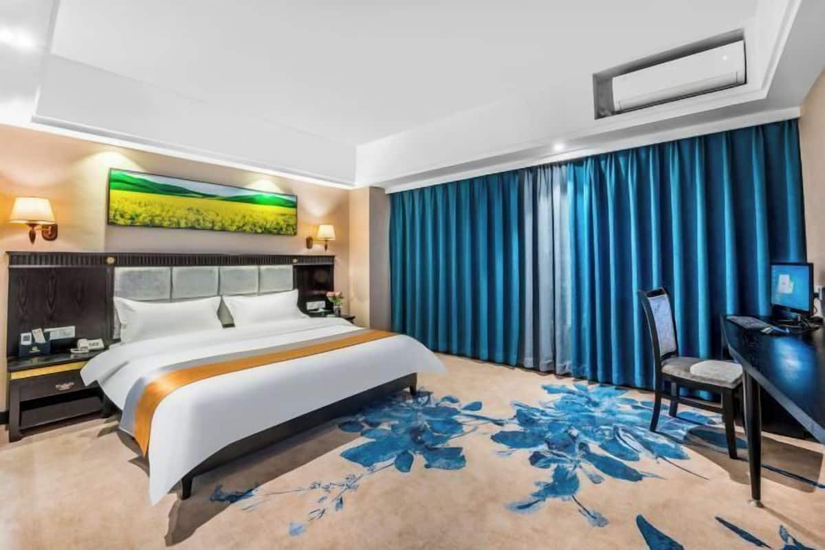 A hotel room with a large bed, a desk, a chair, and a TV.