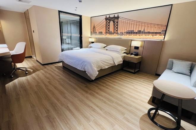 A hotel room with a bed, a desk, a chair, a round table, and a cityscape painting on the wall.