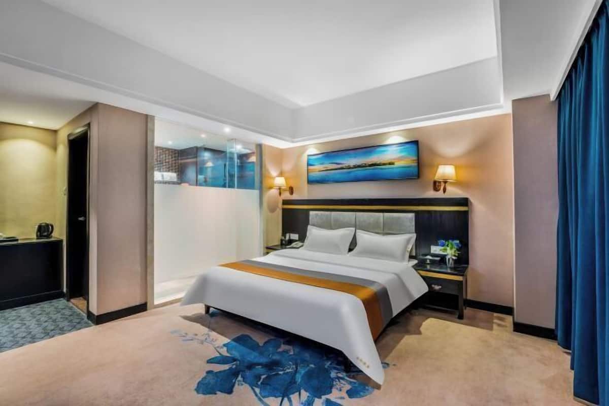 A modern hotel room with a large bed, a nightstand, a desk, and a painting above the bed.