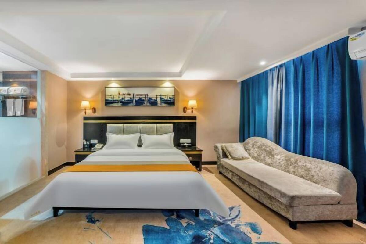 A hotel room with a large bed, a sofa, a nightstand, and a wall-mounted lamp.