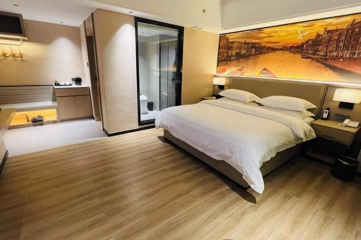 A hotel room with a bed, bedside tables, a shower, and a painting of a cityscape.