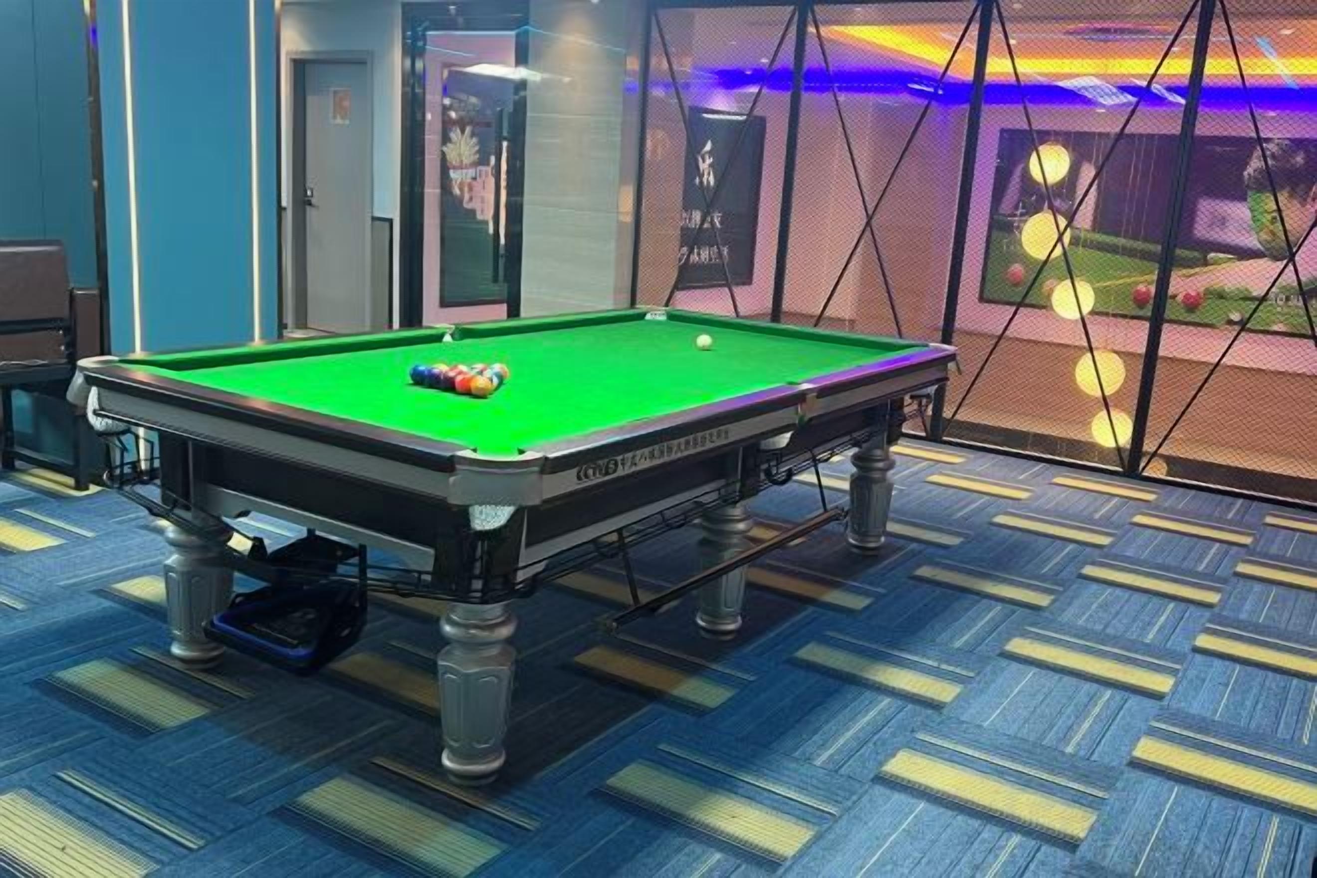 A pool table with balls, a blue carpet, and a room with a door and a wall with a poster.