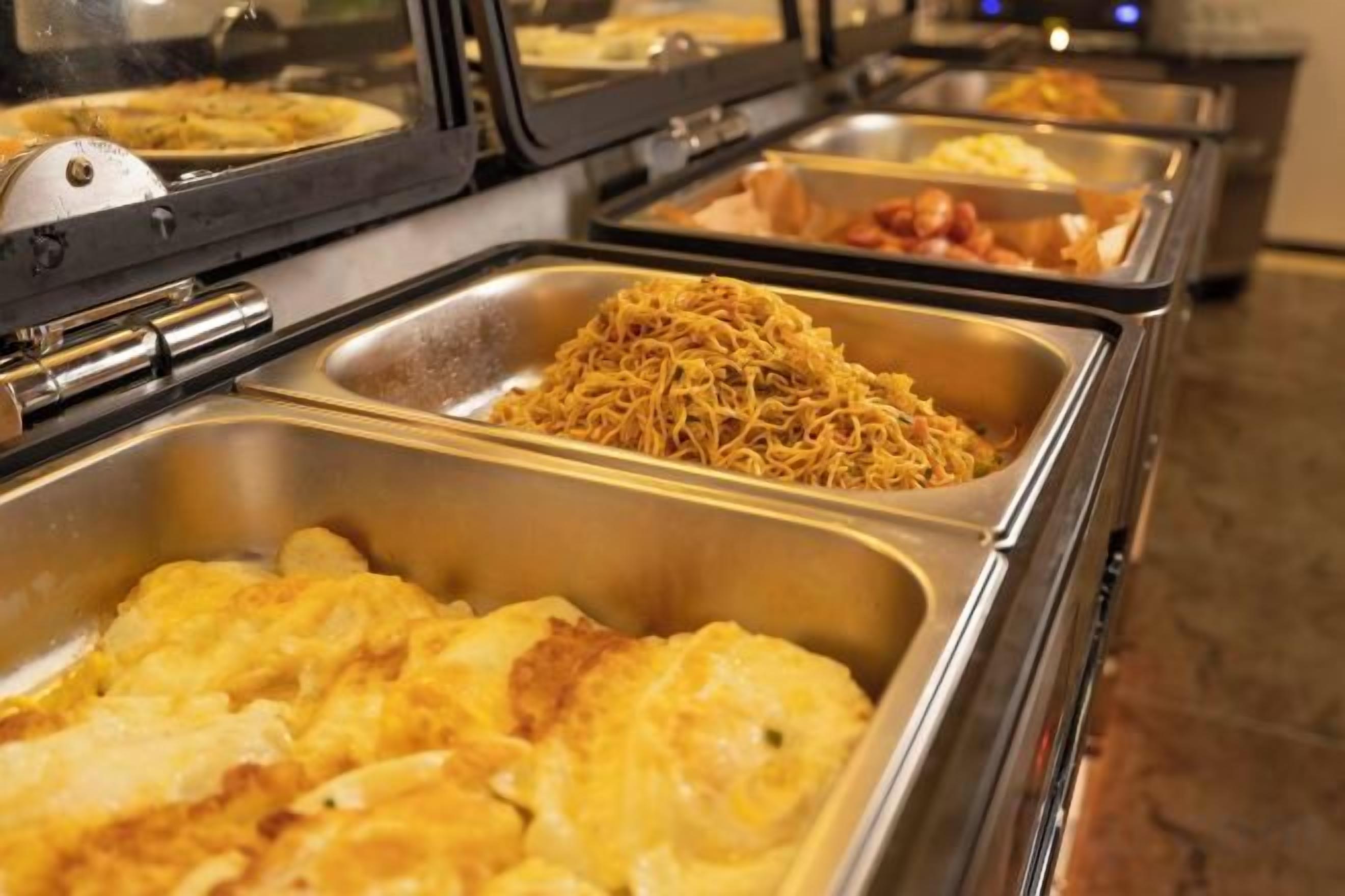 A buffet with various food items in metal serving trays.