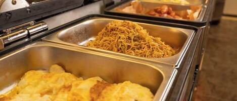 A buffet with various food items in metal serving trays.