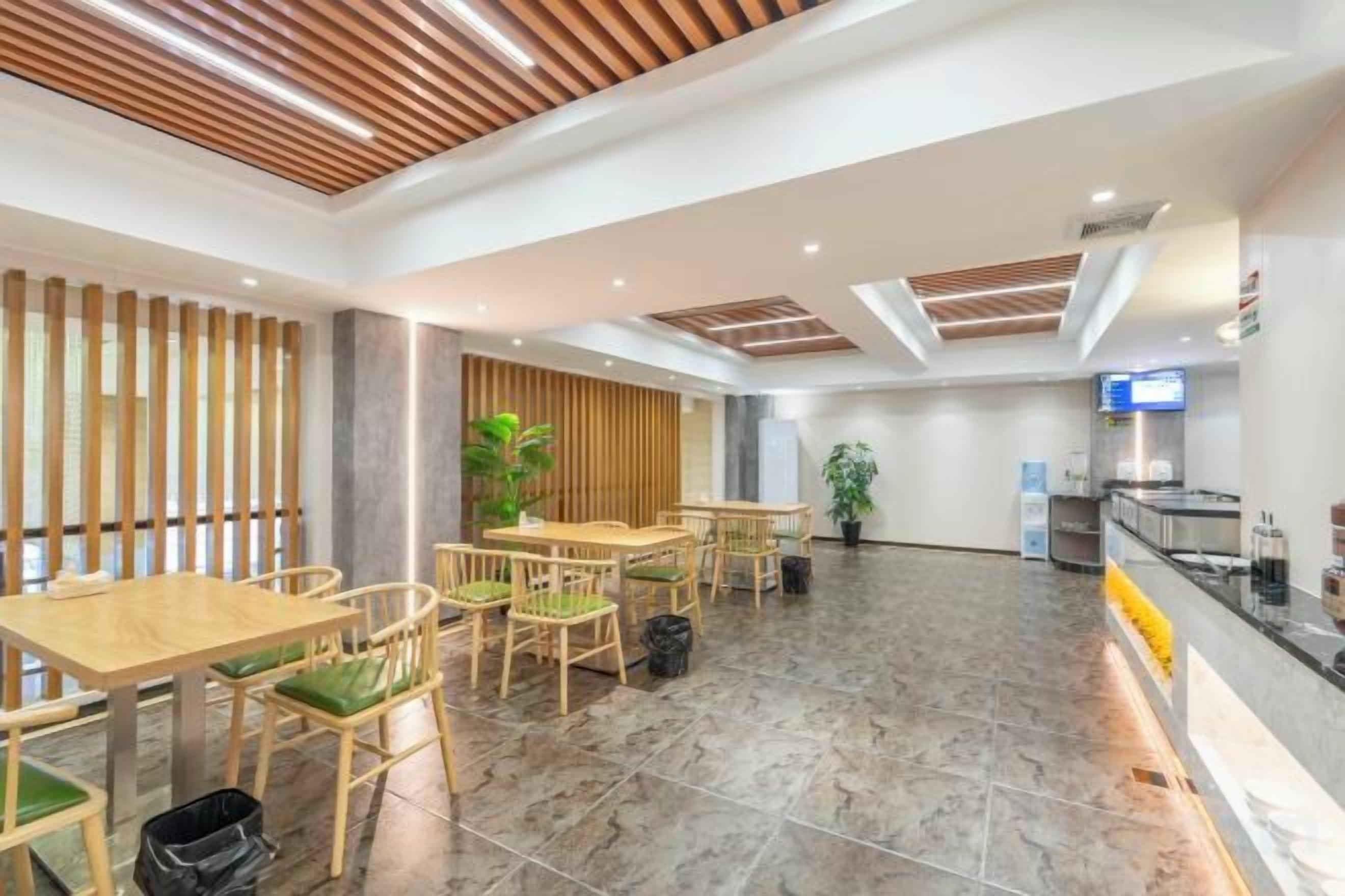 Un espacio interior amplio con varias mesas y sillas de madera, suelo de baldosas y un diseño de techo moderno.