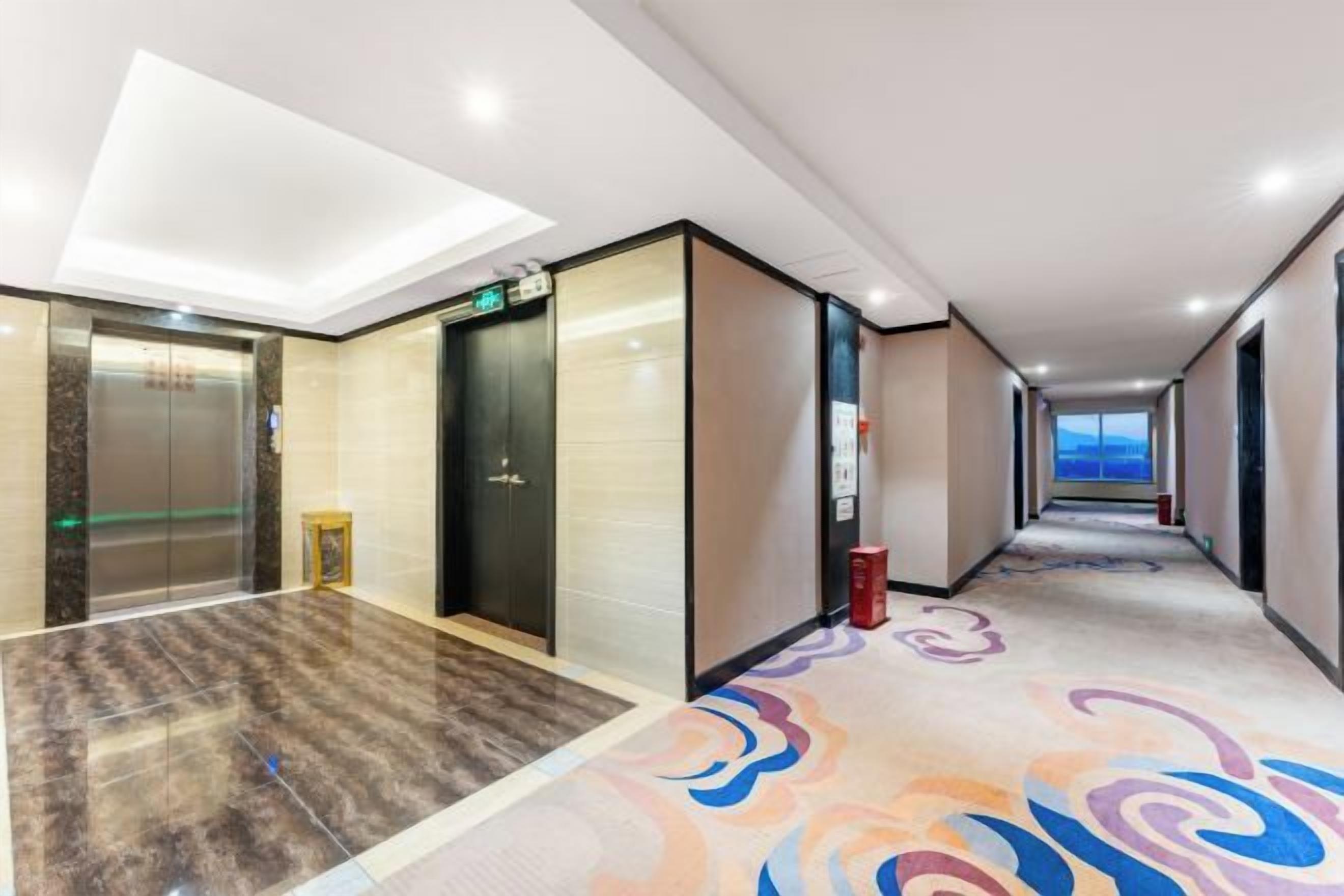 A hotel corridor with elevators, a carpeted floor, and a view of the sky.
