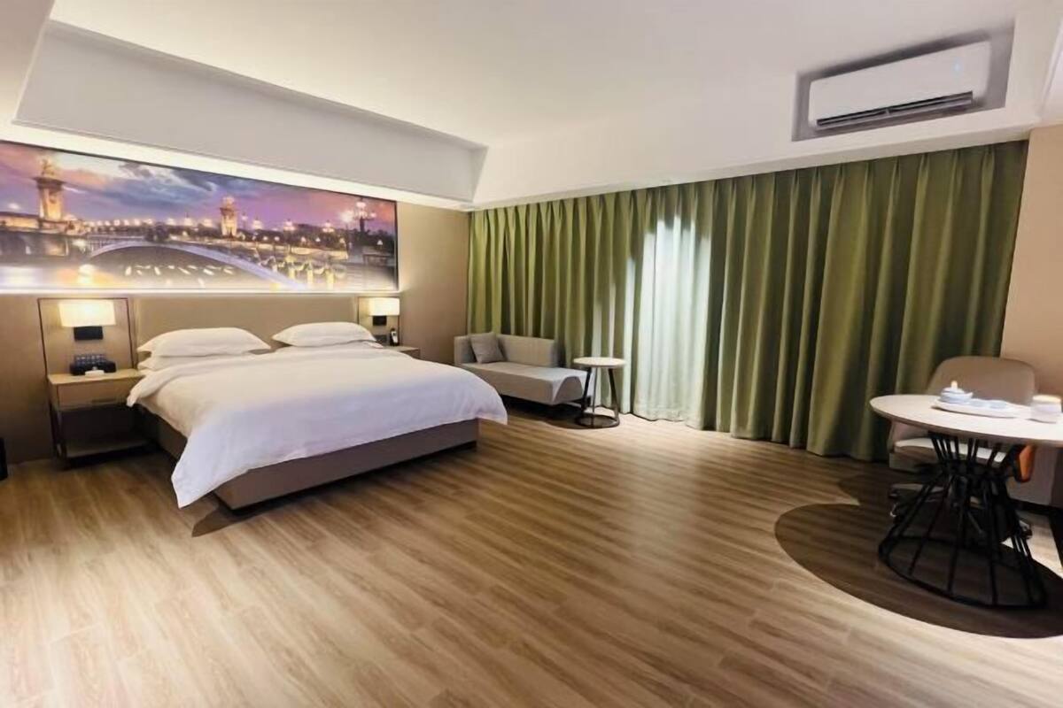 A hotel room with a bed, a sofa, a small table, and a view of a cityscape.