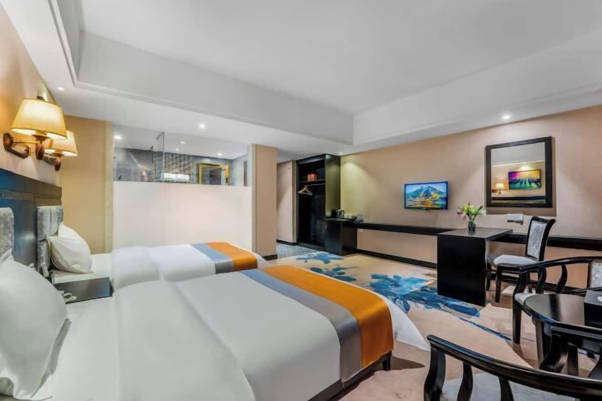 A hotel room with two beds, a desk, a chair, a TV, and a bathroom visible in the background.